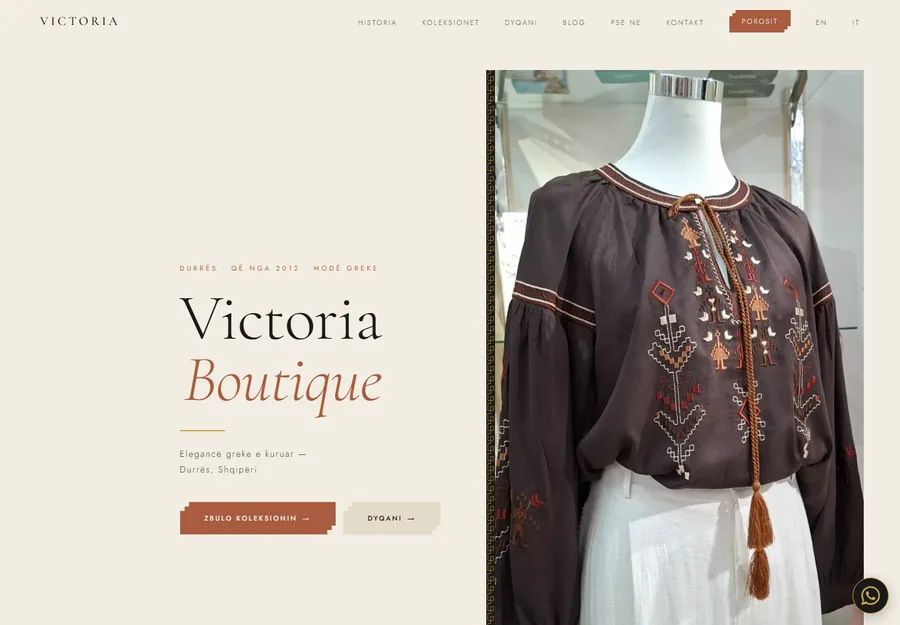 The Victoria Boutique homepage, the wordmark set on limewash beside a Greek embroidered blouse, a meander running down between them